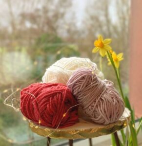 Three balls of wool on a small table by a window with daffodils in the background