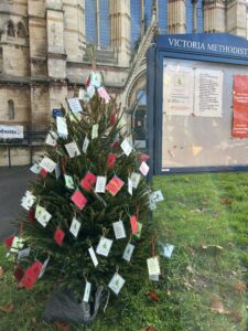 Christmas Tree with lots of labels hanging off it standing outside the church building